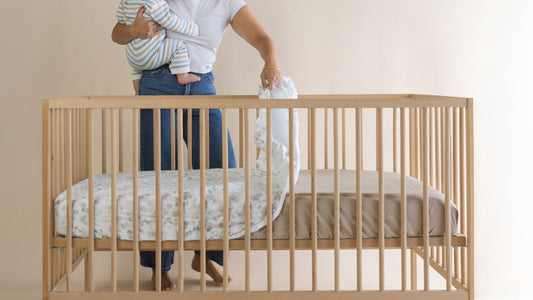 Woman changes cot sheet. Cot complies with current safe sleeping reform. COmpliant product, firmness rated mattress and safe bedding