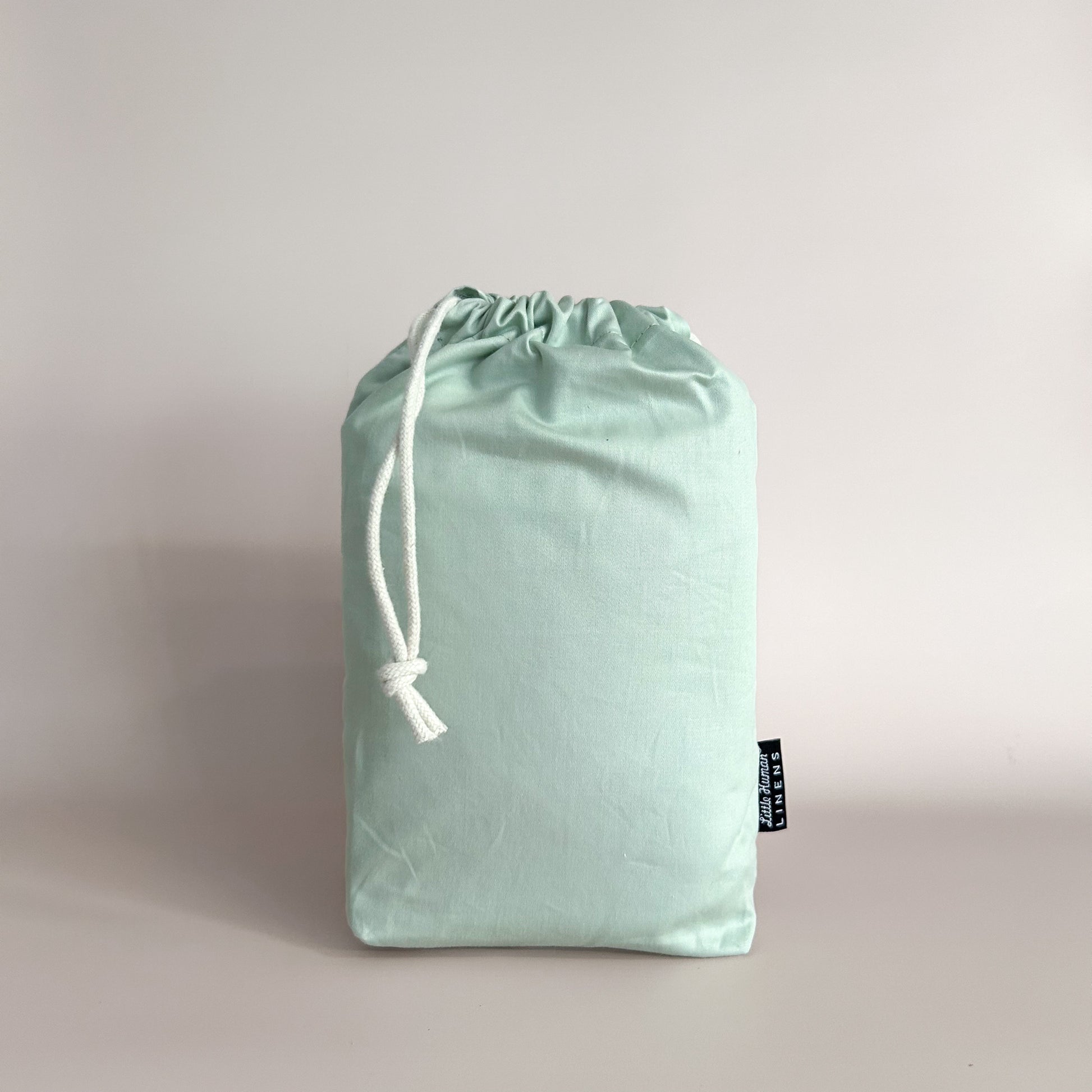 Sage Green Waterproof Co-Sleeper sheet in a sage drawstring bag with a branded label.