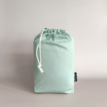 Sage Green Waterproof Co-Sleeper sheet in a sage drawstring bag with a branded label.