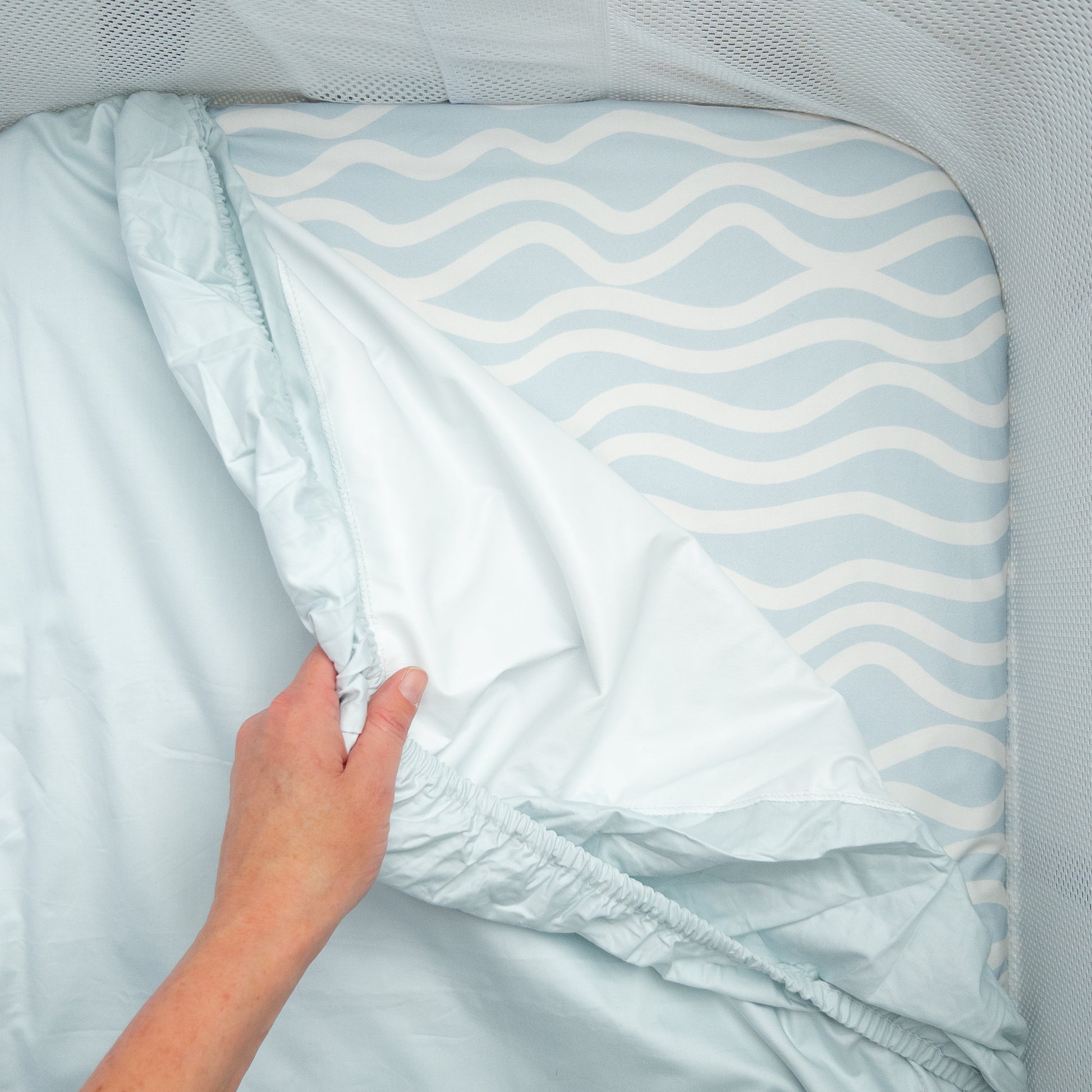 Little Human Linens Bright Waves co-sleeper fitted sheet pulled back to reveal the waterproof layer underneath