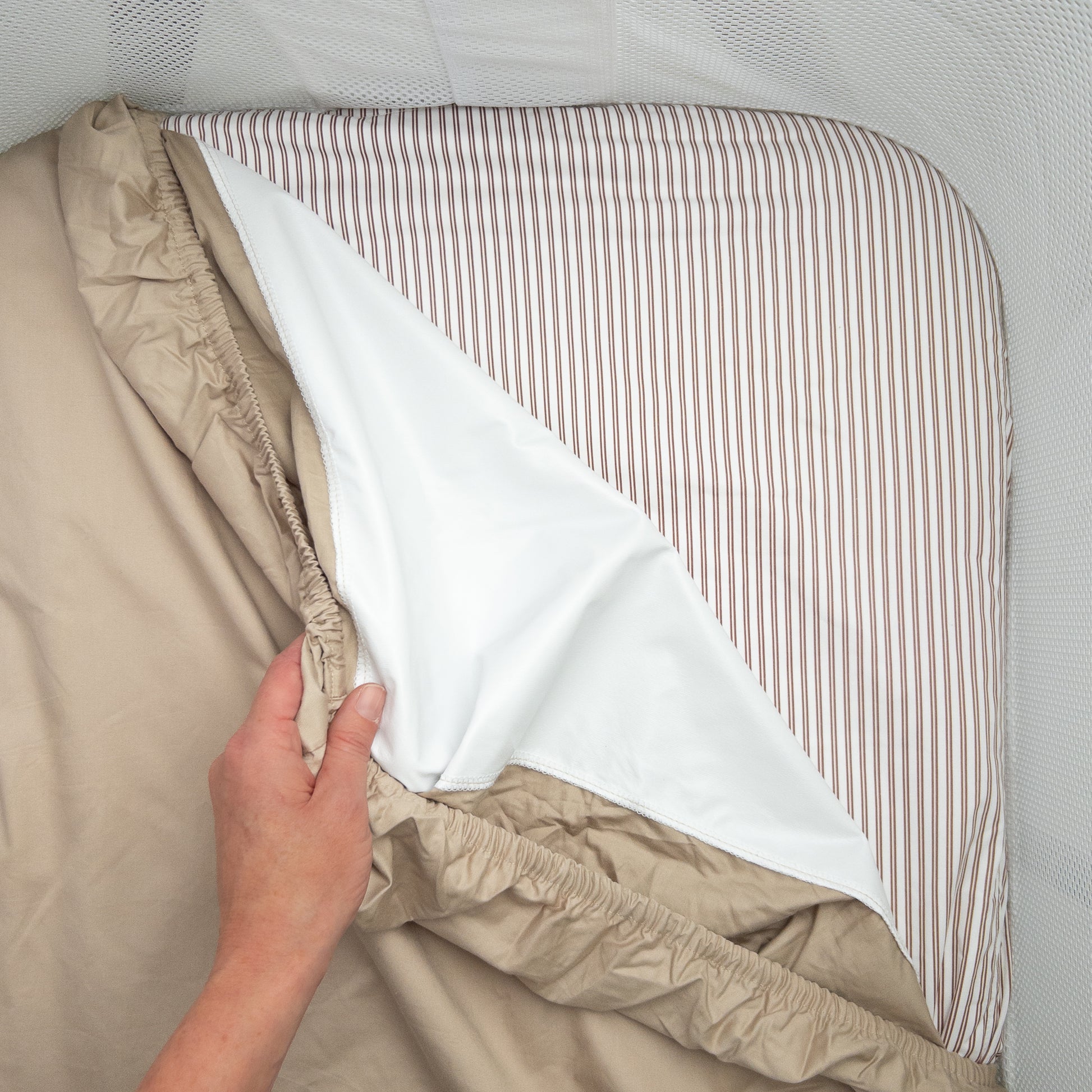Little Human Linens Mocha Pinstripe co-sleeper fitted sheet pulled back to reveal the waterproof layer underneath