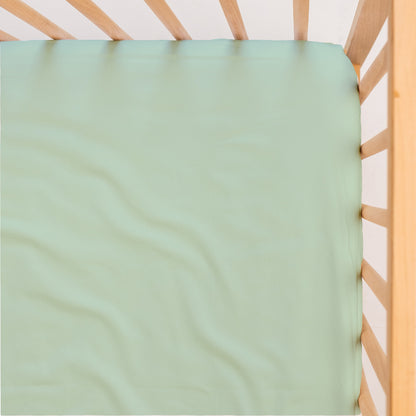 Sage green cot/crib waterproof sheet on a wooden crib with a white background, viewed from above