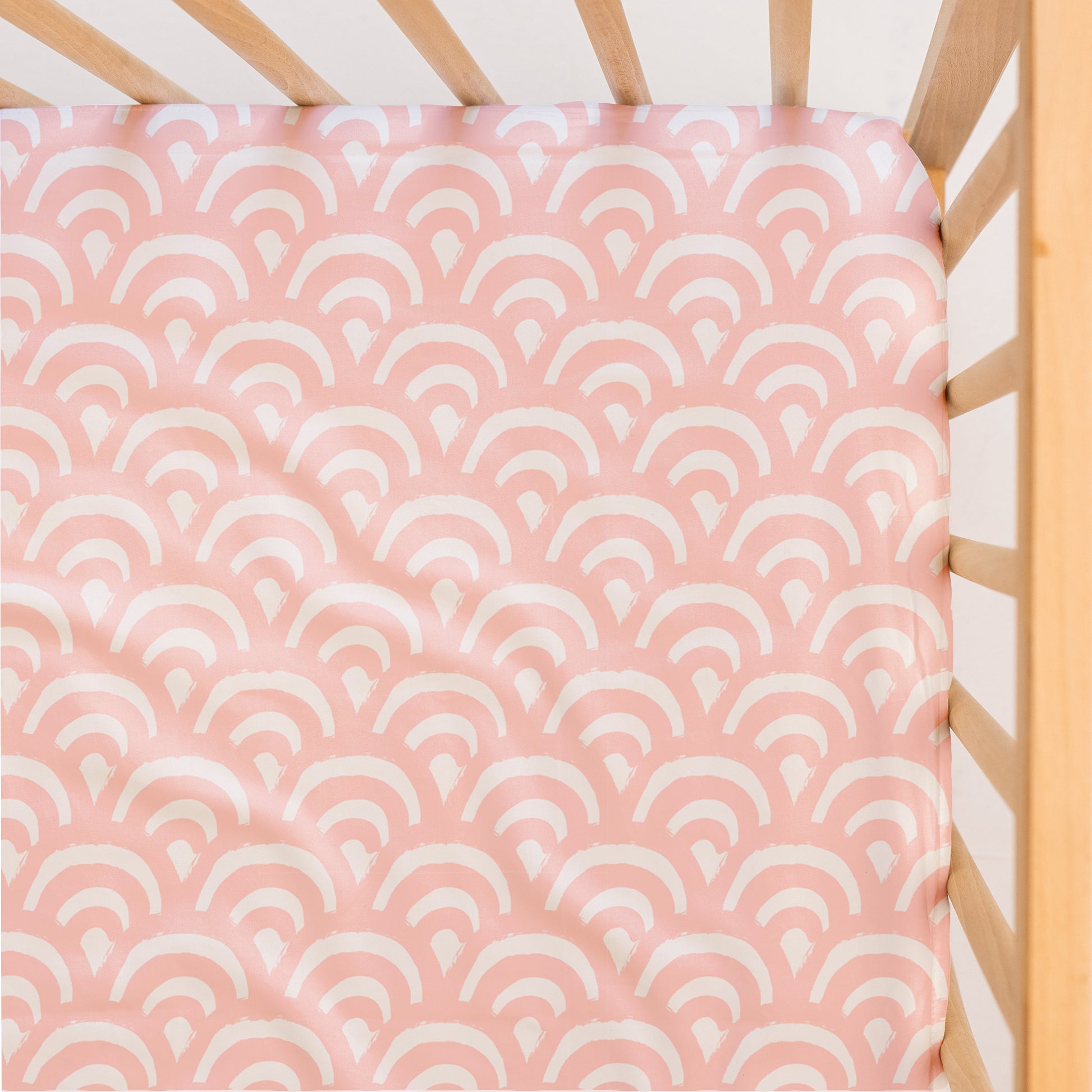 Little Human Linens Peach Rainbows waterproof fitted sheet shown from above, fitted snugly on a standard cot mattress